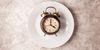 Clock laying on an empty dinner plate representing the OMAD diet