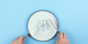 Person cutting up a clock on a blank dinner plate to represent the fasting mimicking diet