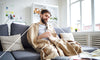 Man wrapped in a blanket and drinking tea while dealing with a cold