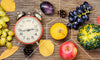 apples, grapes, and berries on a table with a clock representing how long you should fast