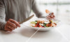 Woman holding a fork and knife and eating from a bowl of foods high in polyamines