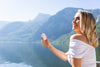 Blond woman holding bottle of spermidineLIFE® over lake in background