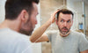 Man looking in mirror and wondering if he can prevent hair loss