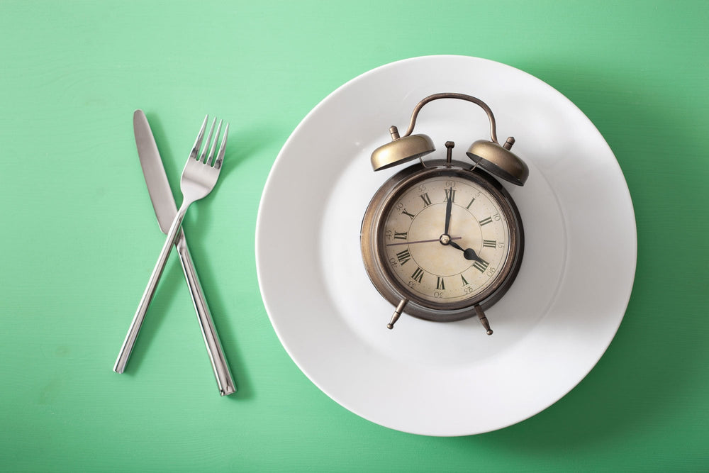 Clock on an empty plate with a fork and knife next to it indicating an intermittent fasting schedule