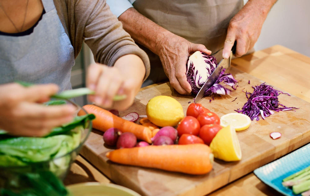 Couple chopping carrots, cabbage, tomatoes, and lemons for a keto diet