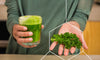 Woman holding a green detox drink that's good for ridding the body of harmful toxins in one hand and parsley in the other