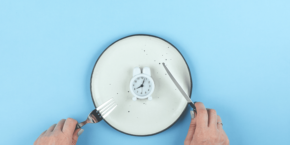 Person cutting up a clock on a blank dinner plate to represent the fasting mimicking diet