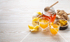 Honey in a jar, whole ginger root, orange juice and lemon peels depicting what is in immune boosting shots